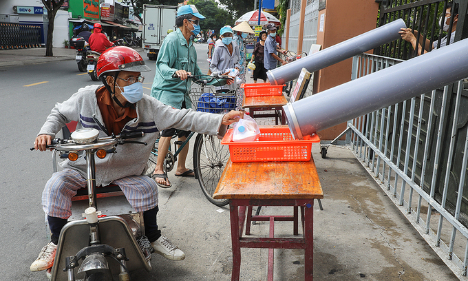 Люди получают бесплатное питание по трубкам, чтобы обеспечить социальное дистанцирование в церкви Тан Са Чау в районе Тан Бинь, Хошимин, 26 июня 2021 года. Фото: VnExpress